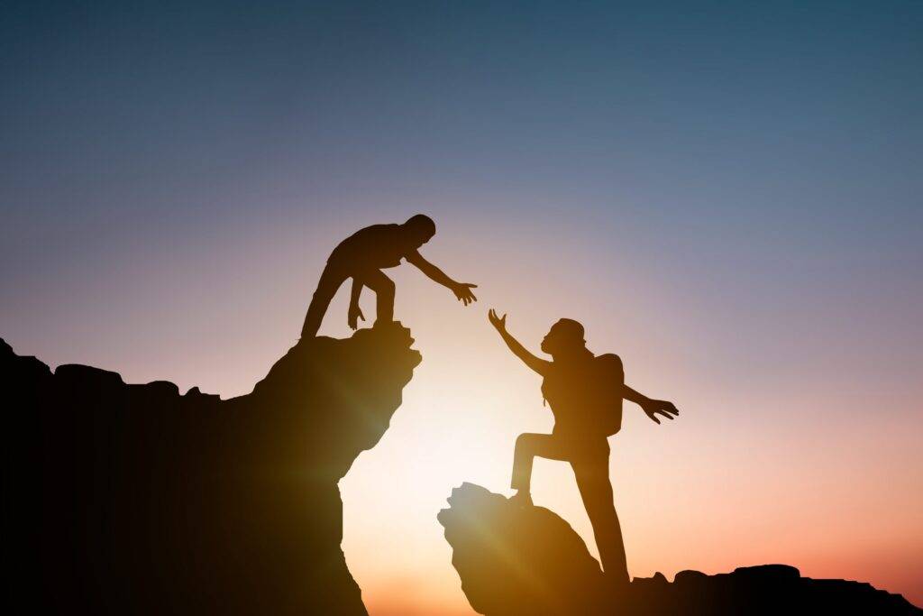 People helping each other climb a rock. Illustration of how to ask for help: reach out.