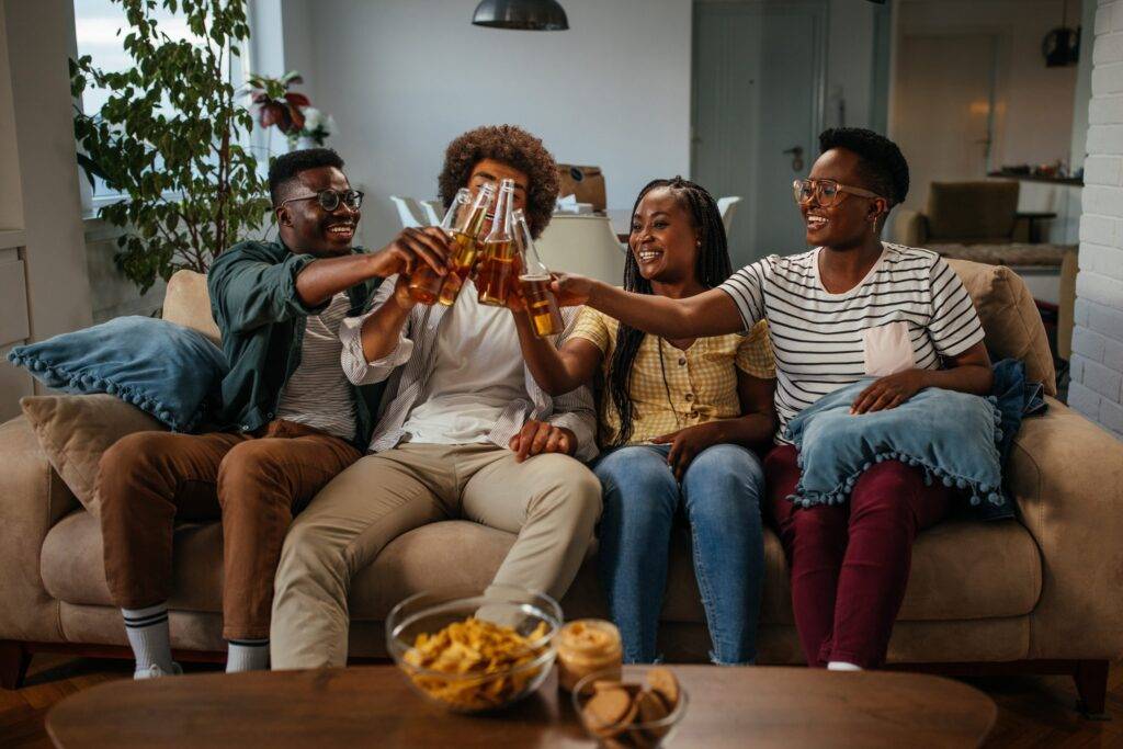 Group of young black friends having beers and snacks in the living room at home
