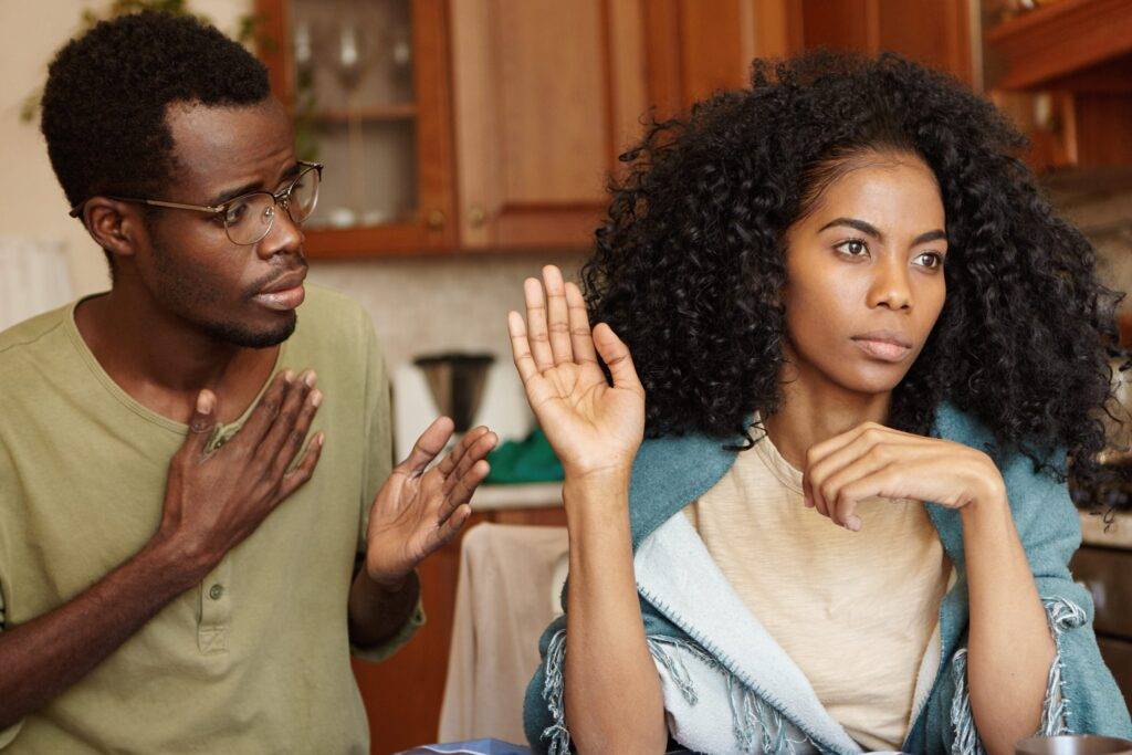 Angry beautiful Afro-American girl feeling mad at her unfaithful husband, ignoring his excuses, not believing in lies. Young couple going through hard times in their relationships