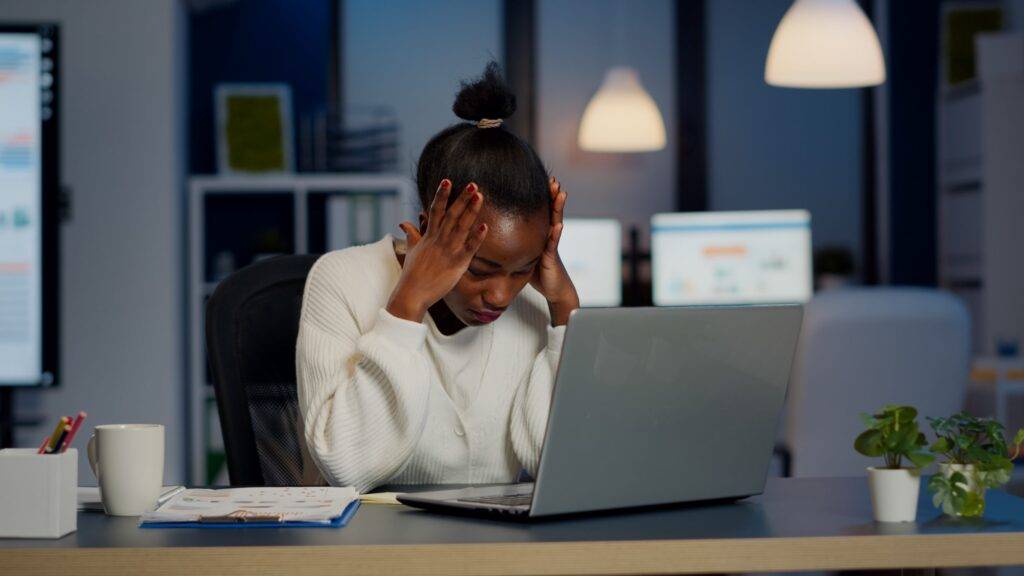 Stressed african businesswoman suffering from headache at work doing overtime late night. 