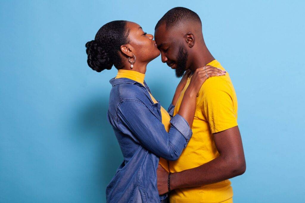 Woman giving boyfriend a kiss on forehead to express love in front of camera. People in relationship showing support.