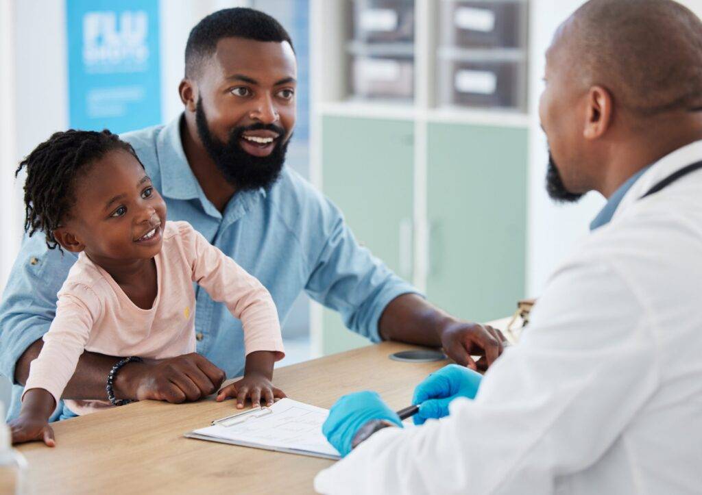 Pediatrician talking to the father of a healthy and happy little girl with ADHD during a checkup at a hospital.