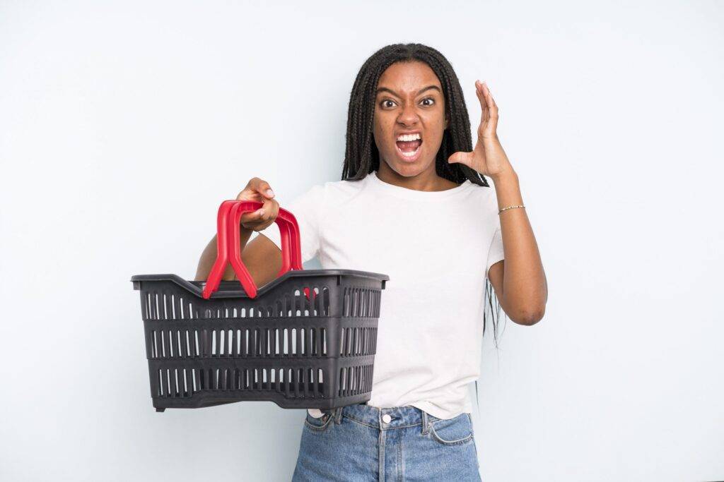 Pretty black woman with an empty shopping basket screaming with hands up in the air.